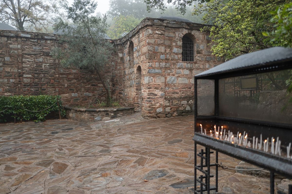 Lit prayer candles in a covered stand in the stone courtyard of the House of Virgin Mary near Ephesus, on a misty day