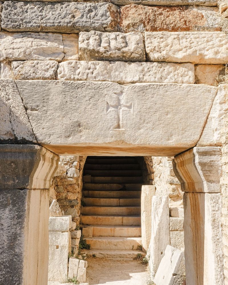 A cross carved into the stone lintel above a side entrance of the Great Theater at Ephesus, with steps rising into the passage below
