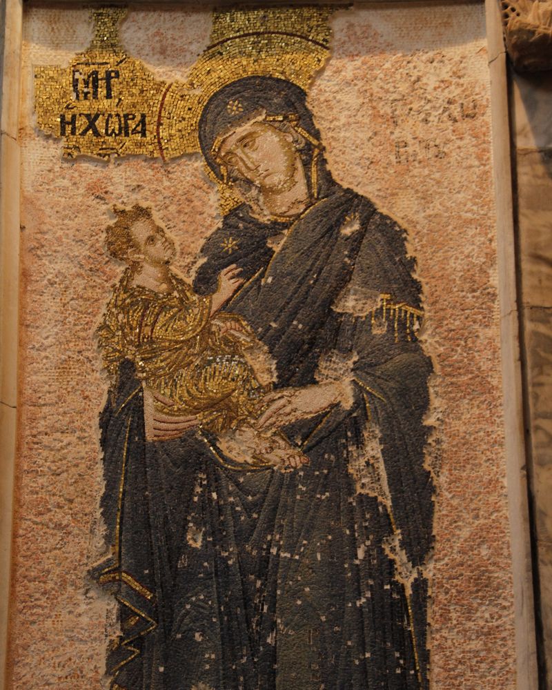 Byzantine mosaic of the Virgin Mary in a dark blue robe holding the child Jesus in gold, with a gold Greek inscription beside her head, at the Chora Church in Istanbul